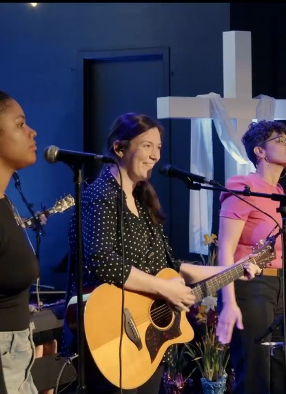 Worship vocalists with acoustic guitar in front of the cross